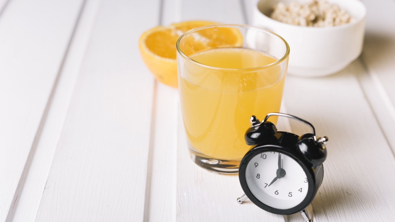 Черный будильник на столе со стаканом сока и хлопьями 