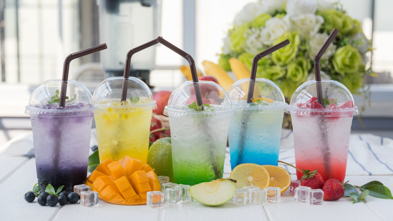 Коктейли в стаканах с трубочками на столе с кубиками льда и фруктами