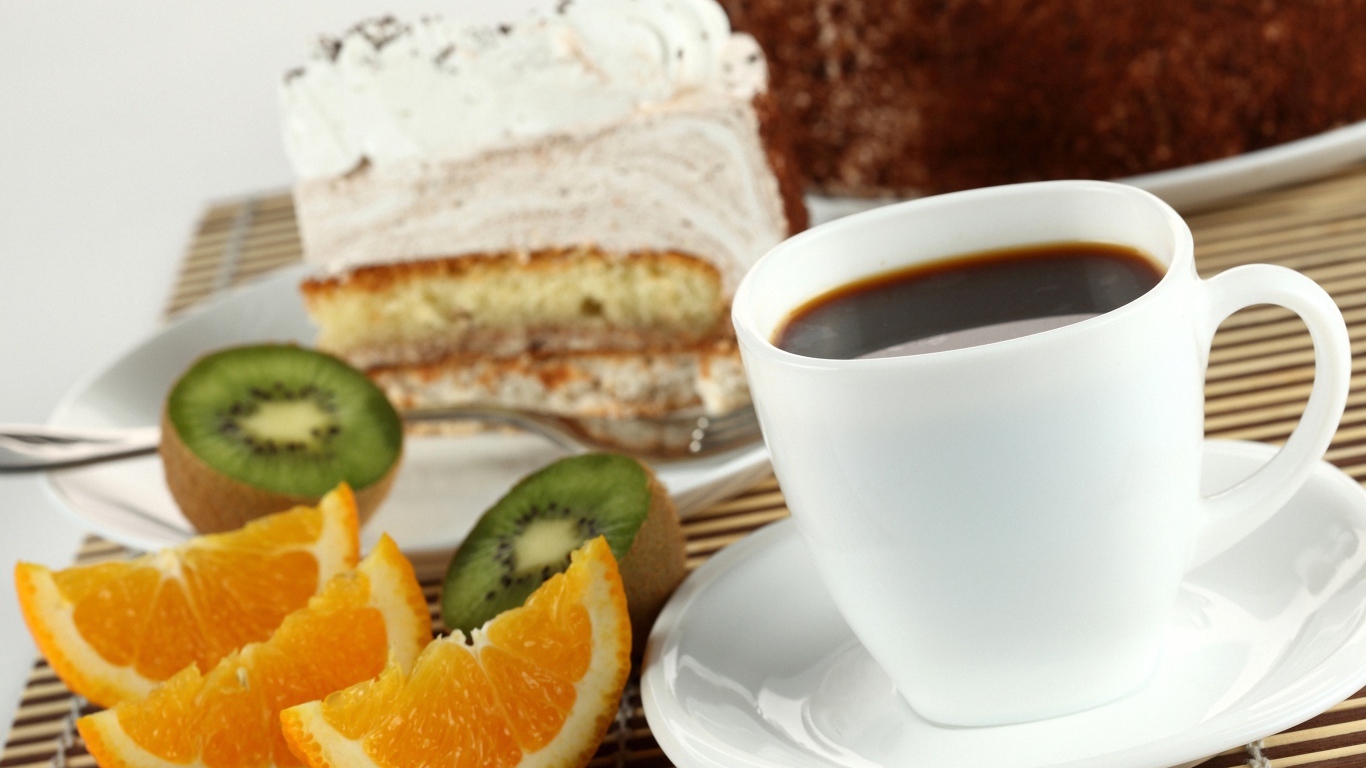 Кофе с куском торта и кусочками апельсина и киви на столе