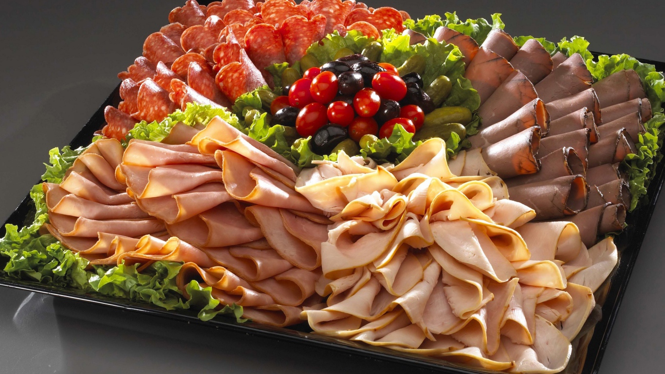 Большое блюдо с аппетитной мясной нарезкой, листьями салата и оливками