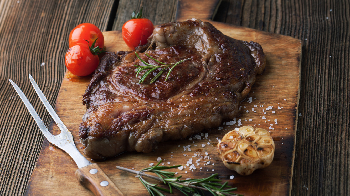 Кусок жареного мяса на разделочной доске с помидорами и чесноком