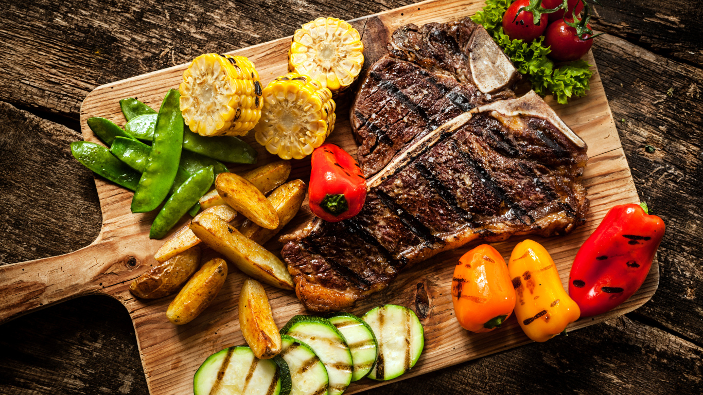 Кусок мяса на разделочной доске с овощами