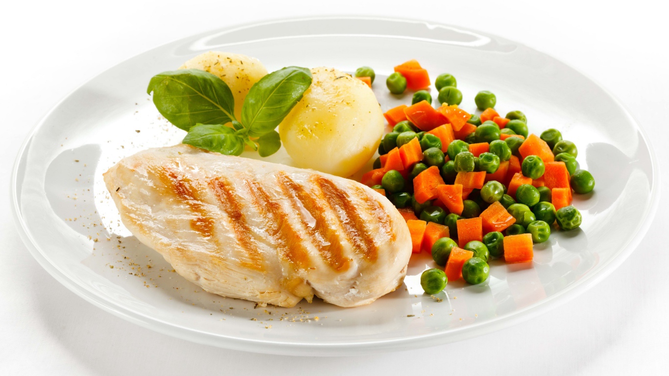 Куриная грудка на белой тарелке с картофелем, морковью и зеленым горошком