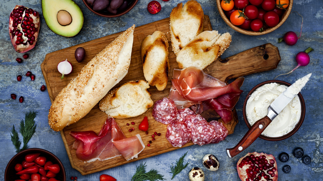 Мясные продукты с батоном и овощами на столе