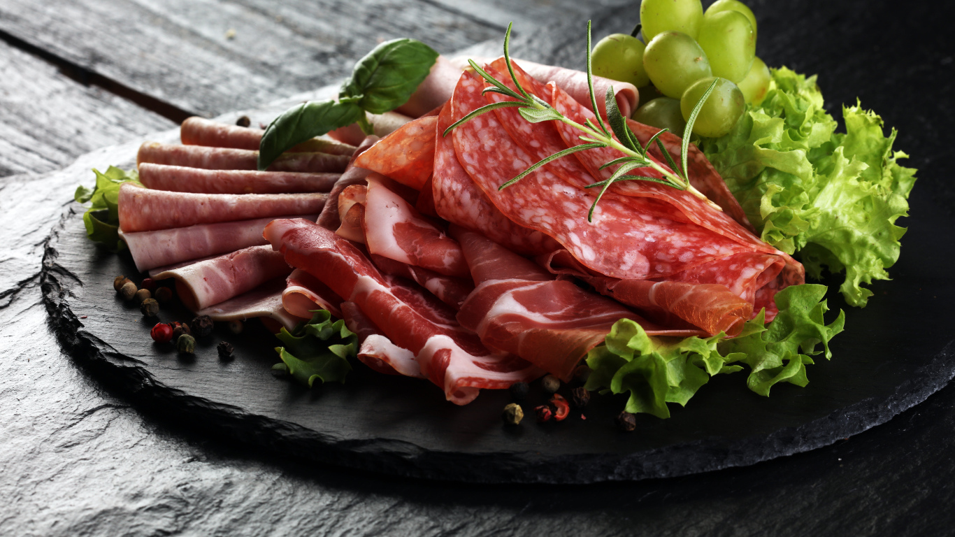 Мясная нарезка с листьями салата и белым виноградом 