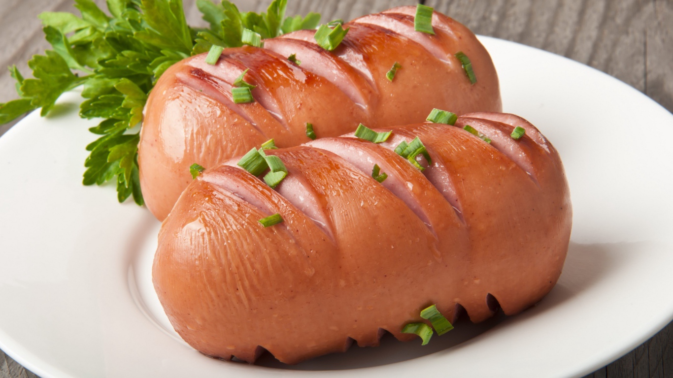 Два жареные сардельки на большой белой тарелке с зеленью 