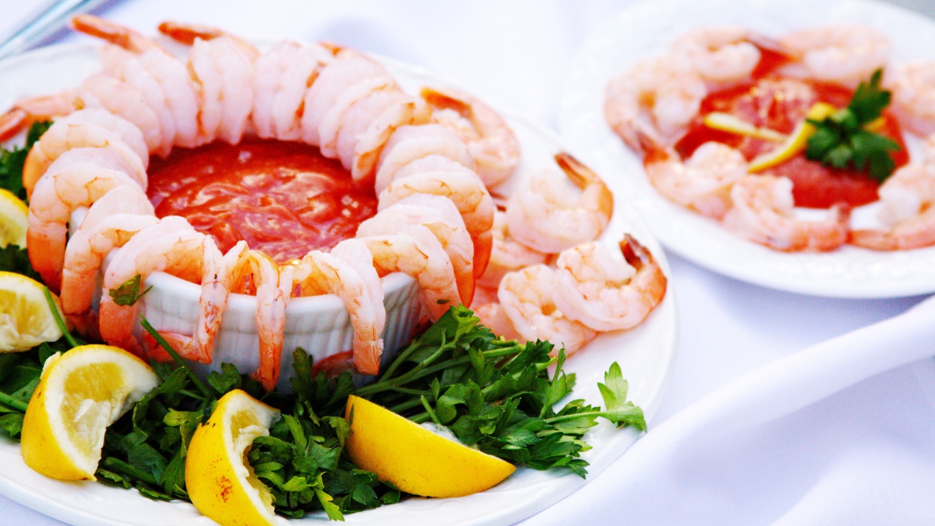 Вареные креветки с соусом на тарелке с лимоном и зеленью петрушки 