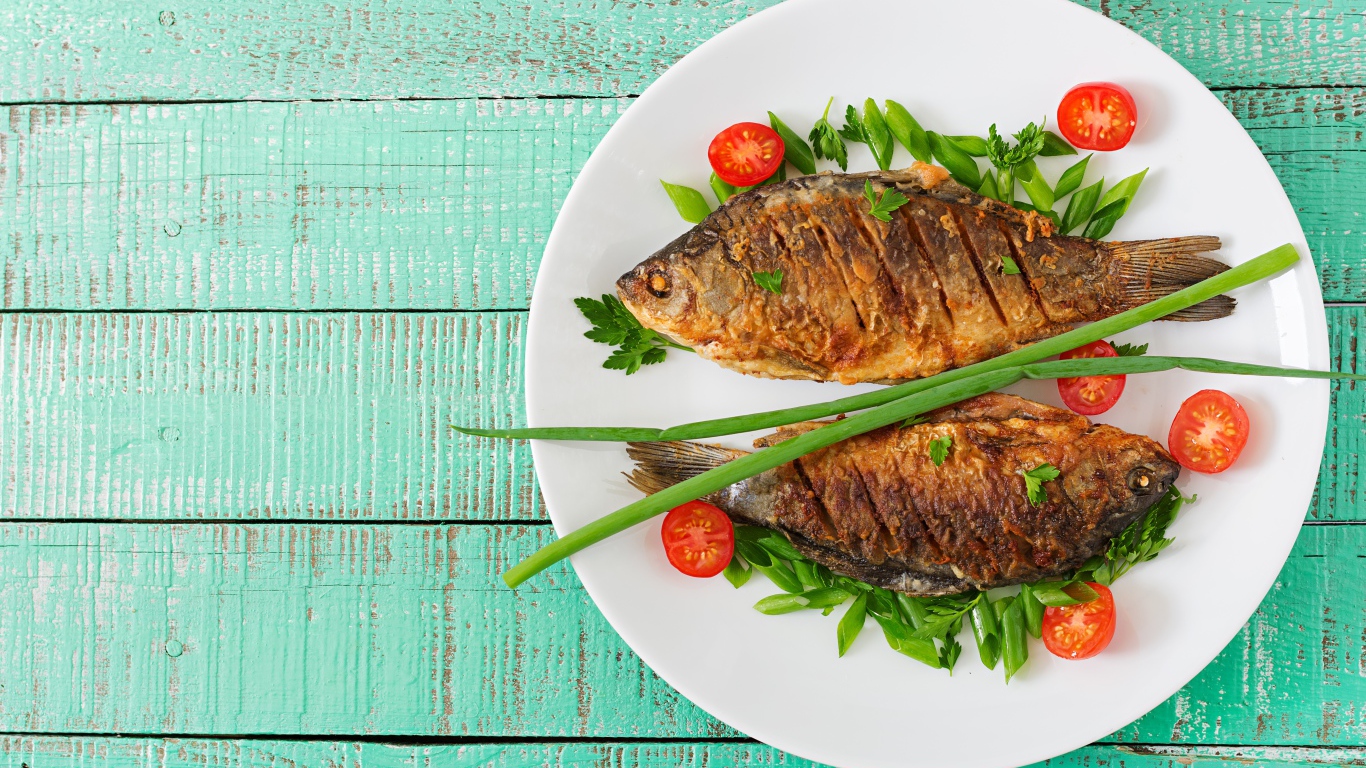 Жареная рыба с помидорами и зеленью на столе