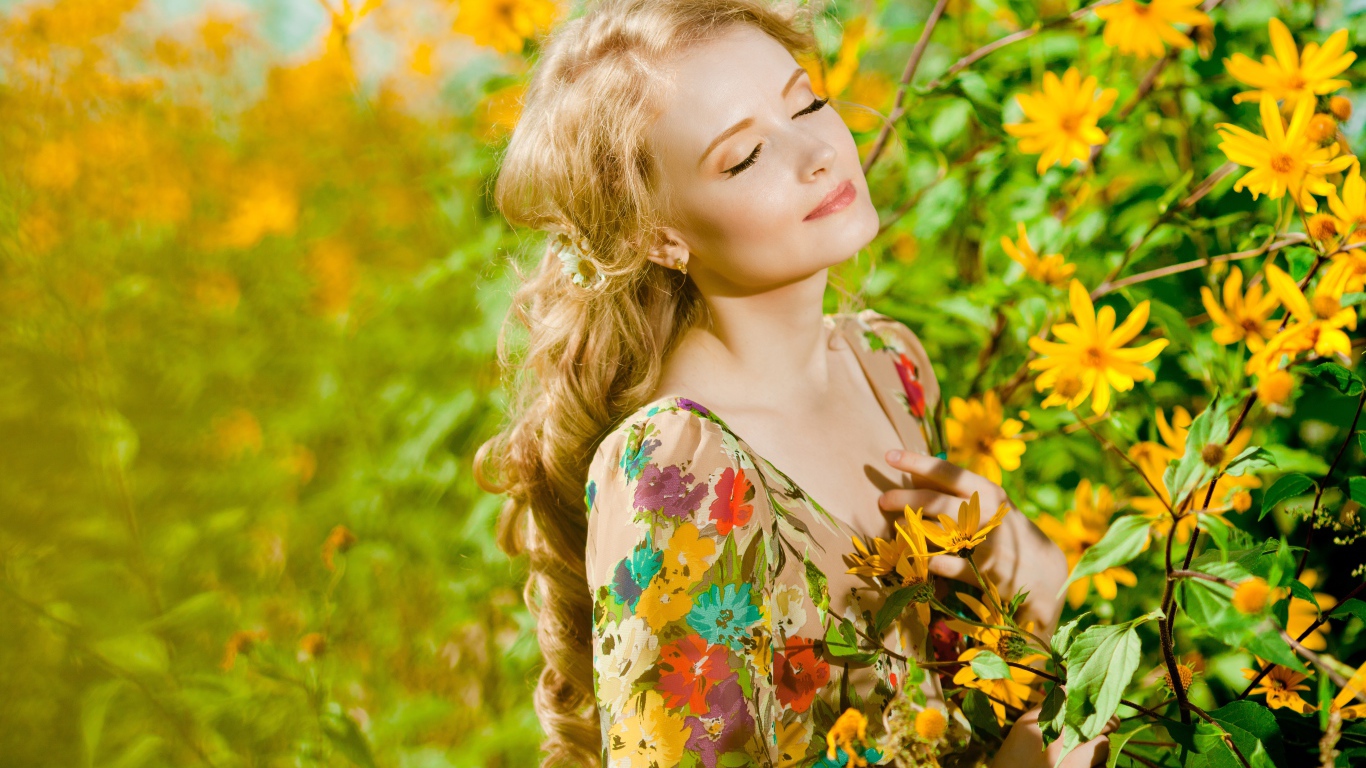 Красивая блондинка нежится в лучах солнца у желтых цветов