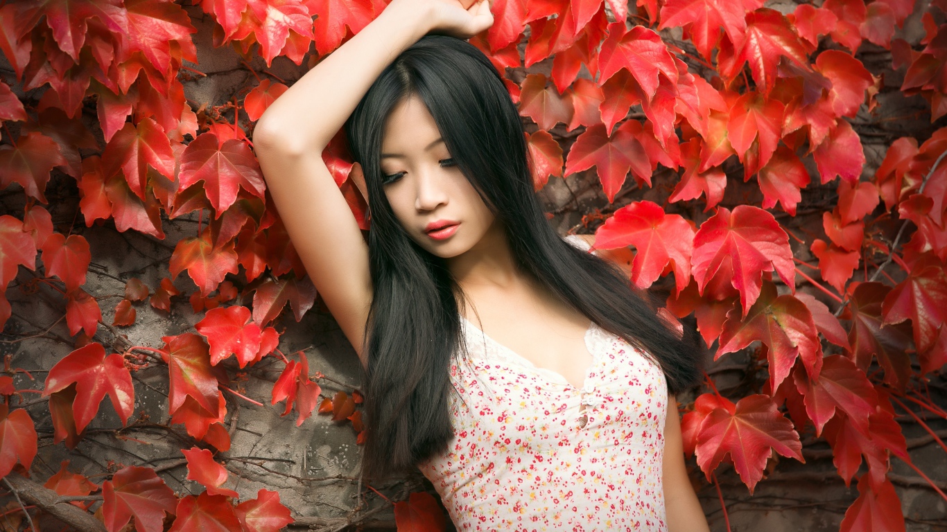 Молодая девушка азиатка стоит у стены с красными листьями