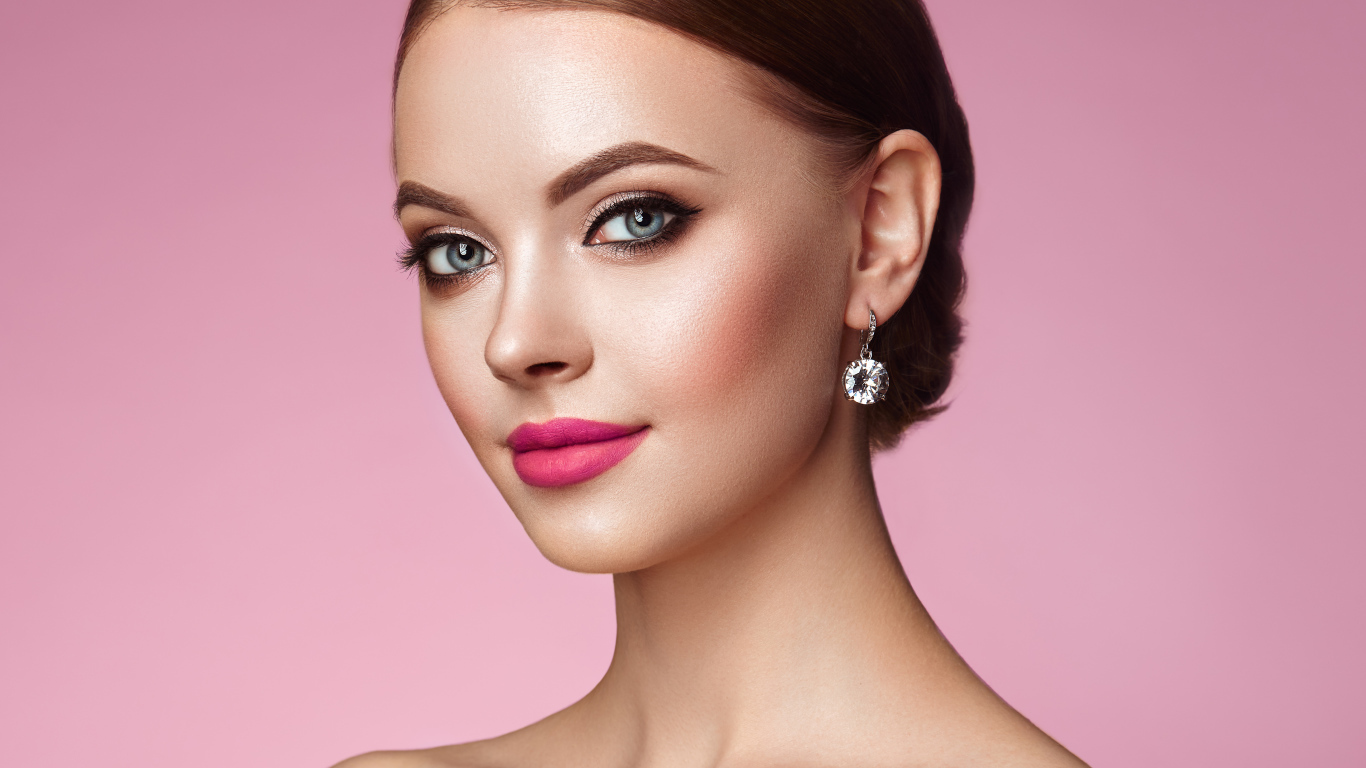 Красивая голубоглазая девушка с красивыми серьгами на розовом фоне