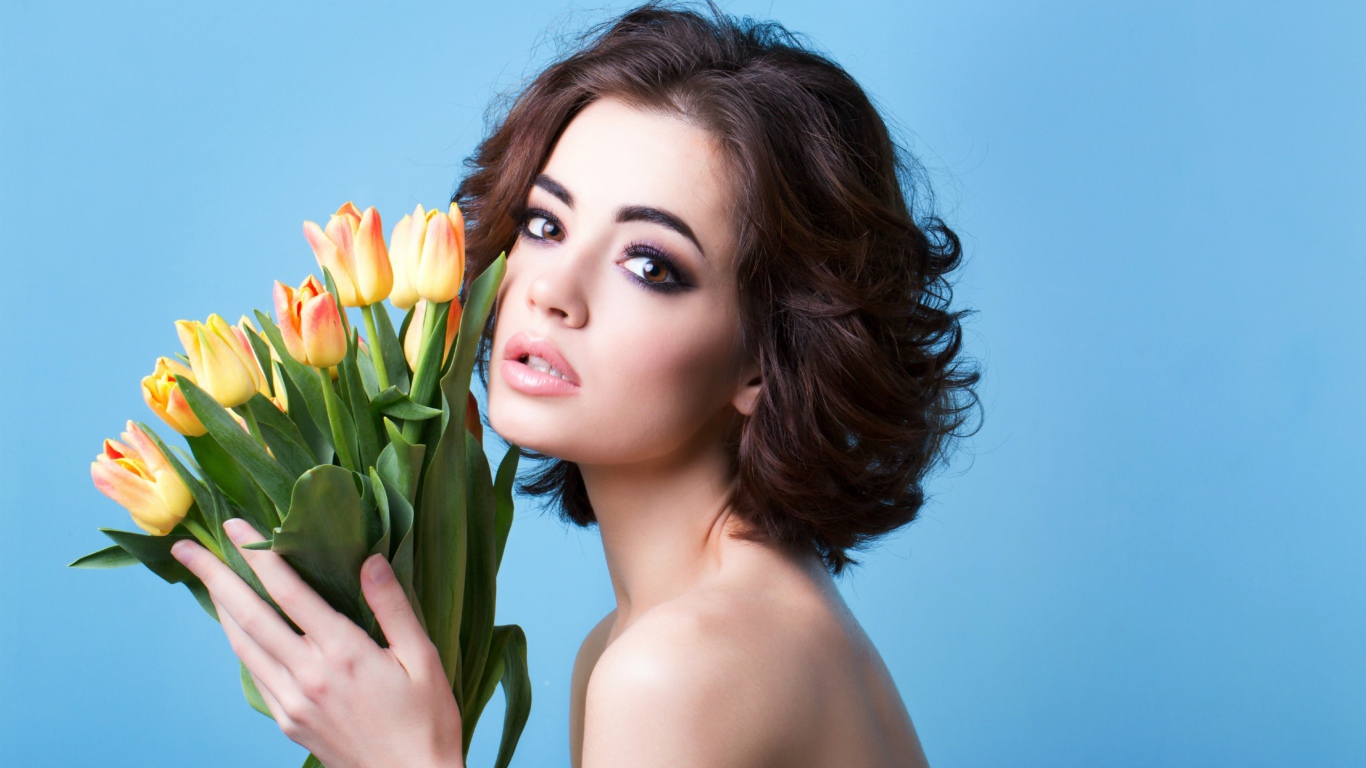 Красивая девушка брюнетка с букетом тюльпанов на голубом фоне
