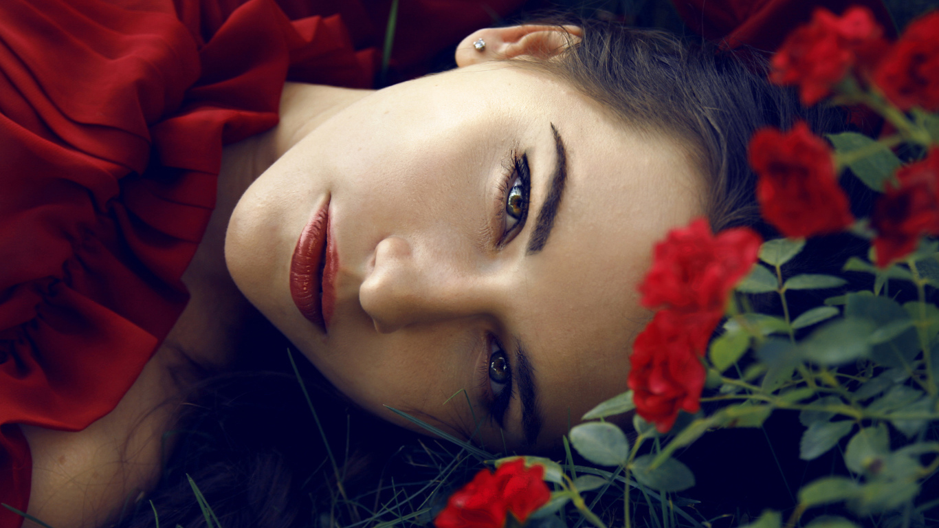 Красивая брюнетка лежит на траве с красными розами