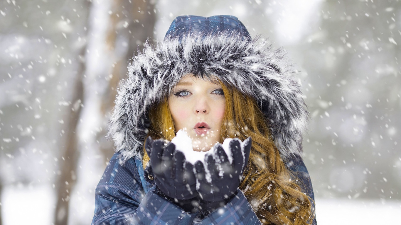 Красивая девушка в теплой куртке со снегом в руках
