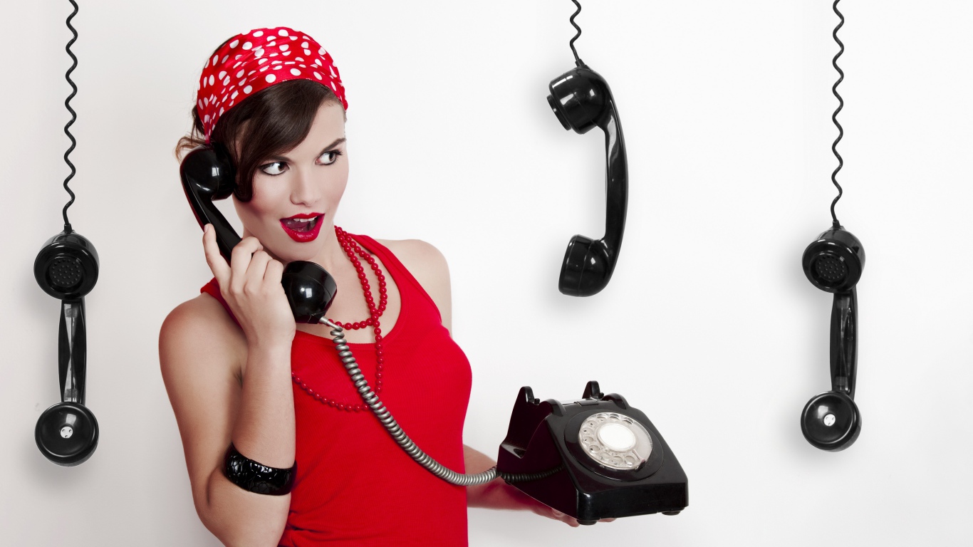 Красивая девушка в красном с черным старым телефоном в руках