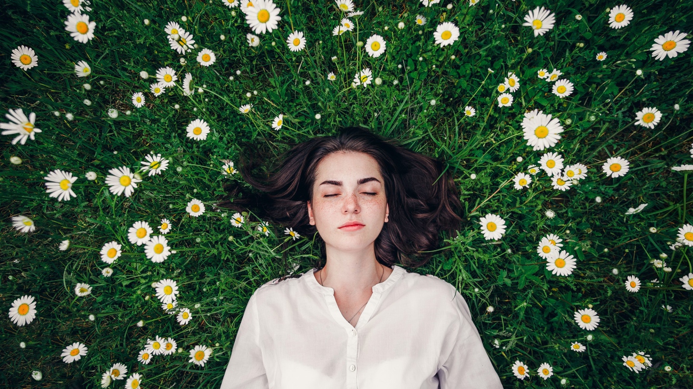 Красивая девушка лежит на зеленой траве с ромашками