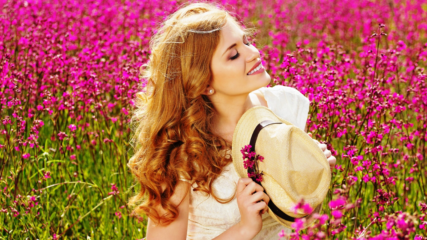 Красивая девушка с шляпой в руках на поле с розовыми цветами