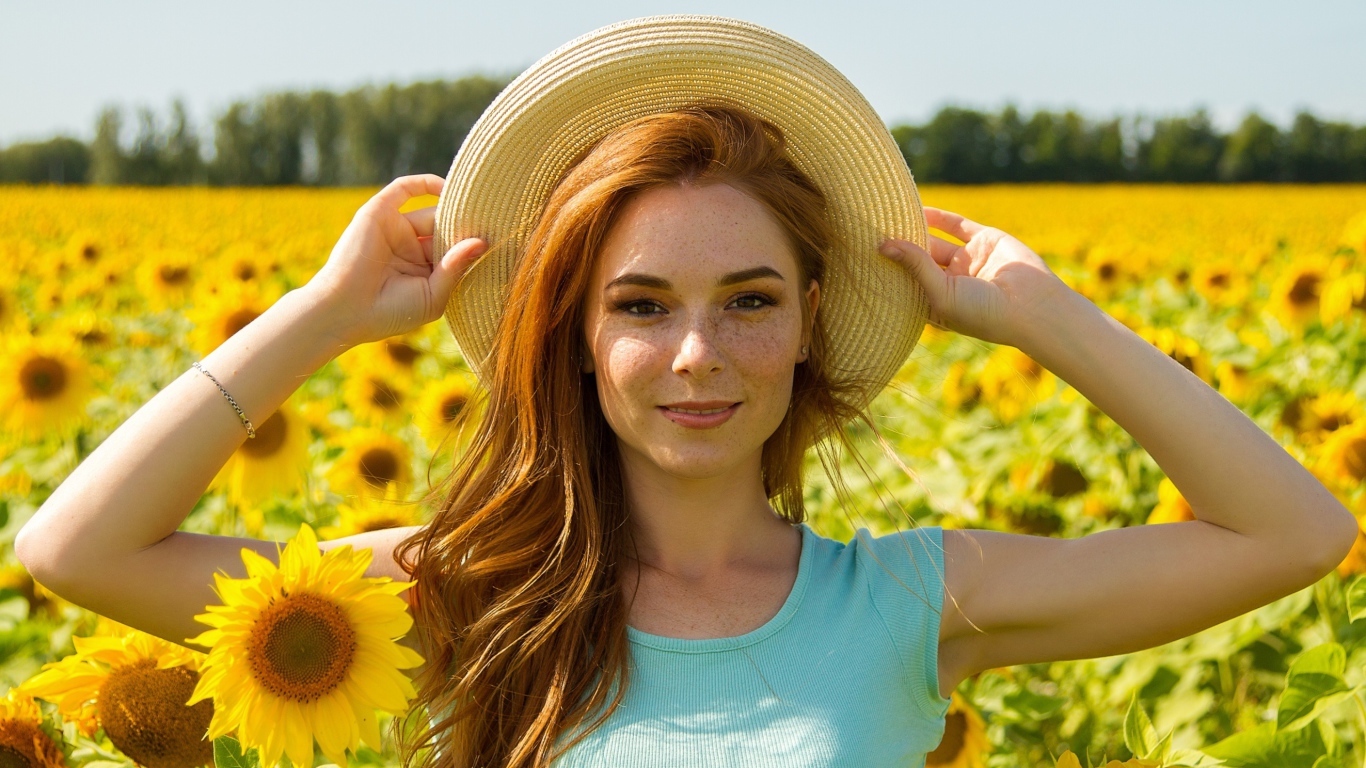 Красивая рыжеволосая девушка в шляпе на поле с подсолнухами 