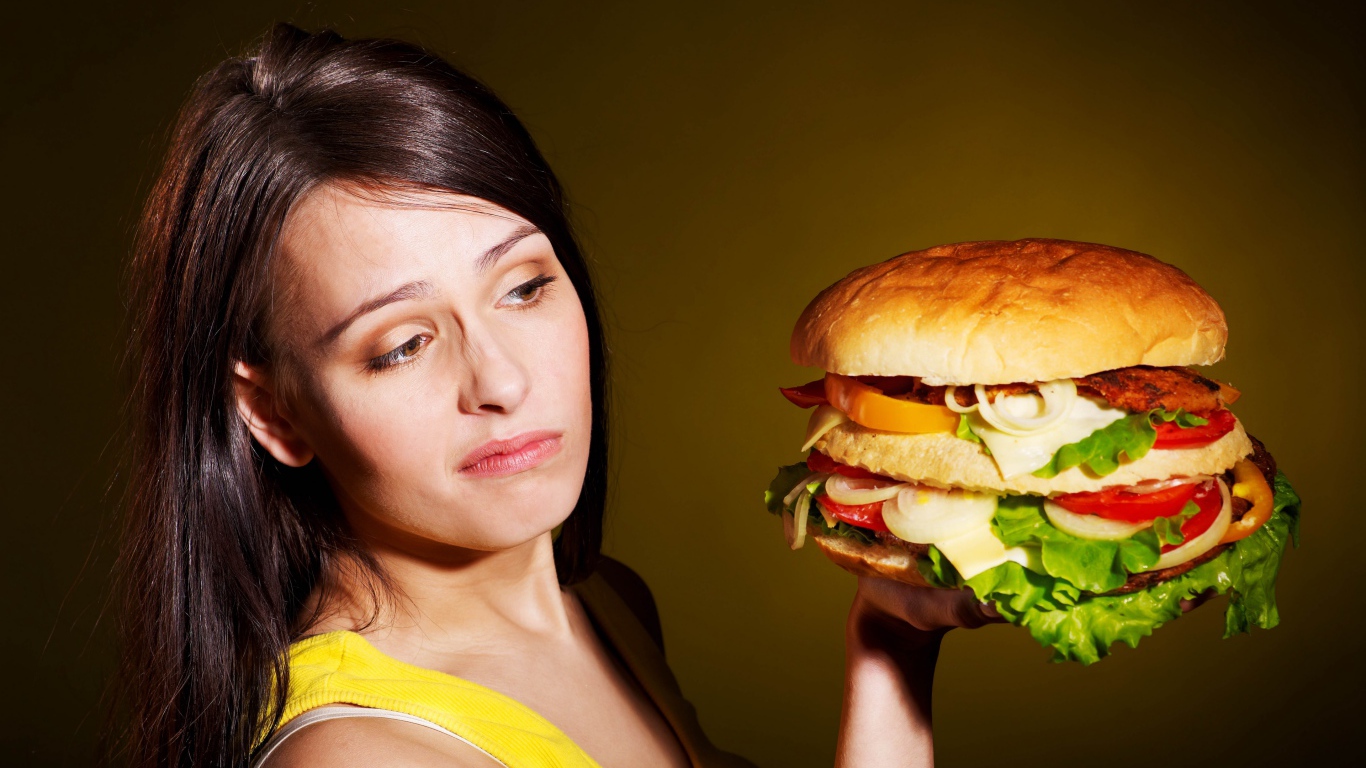 Недовольная девушка с большим гамбургером в руках 