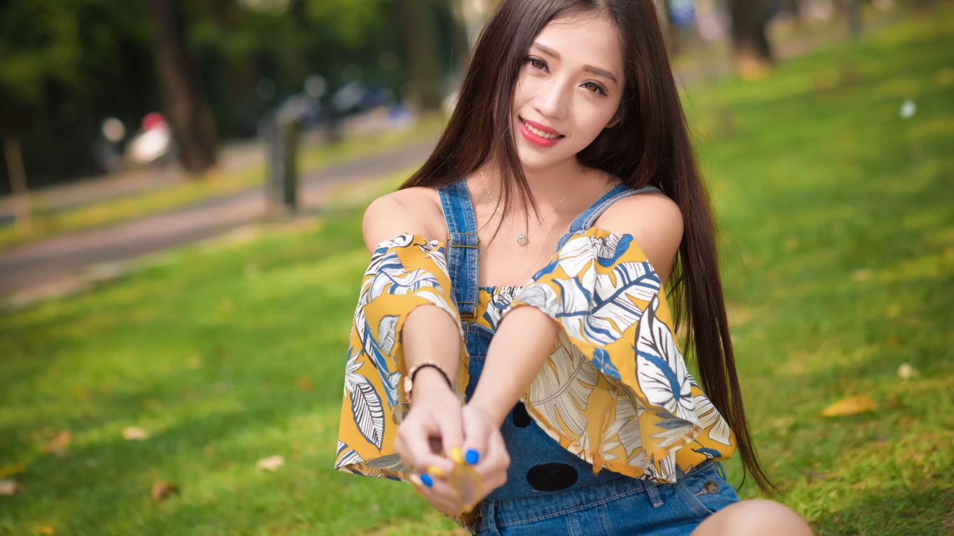 Улыбающаяся девушка азиатка сидит на траве