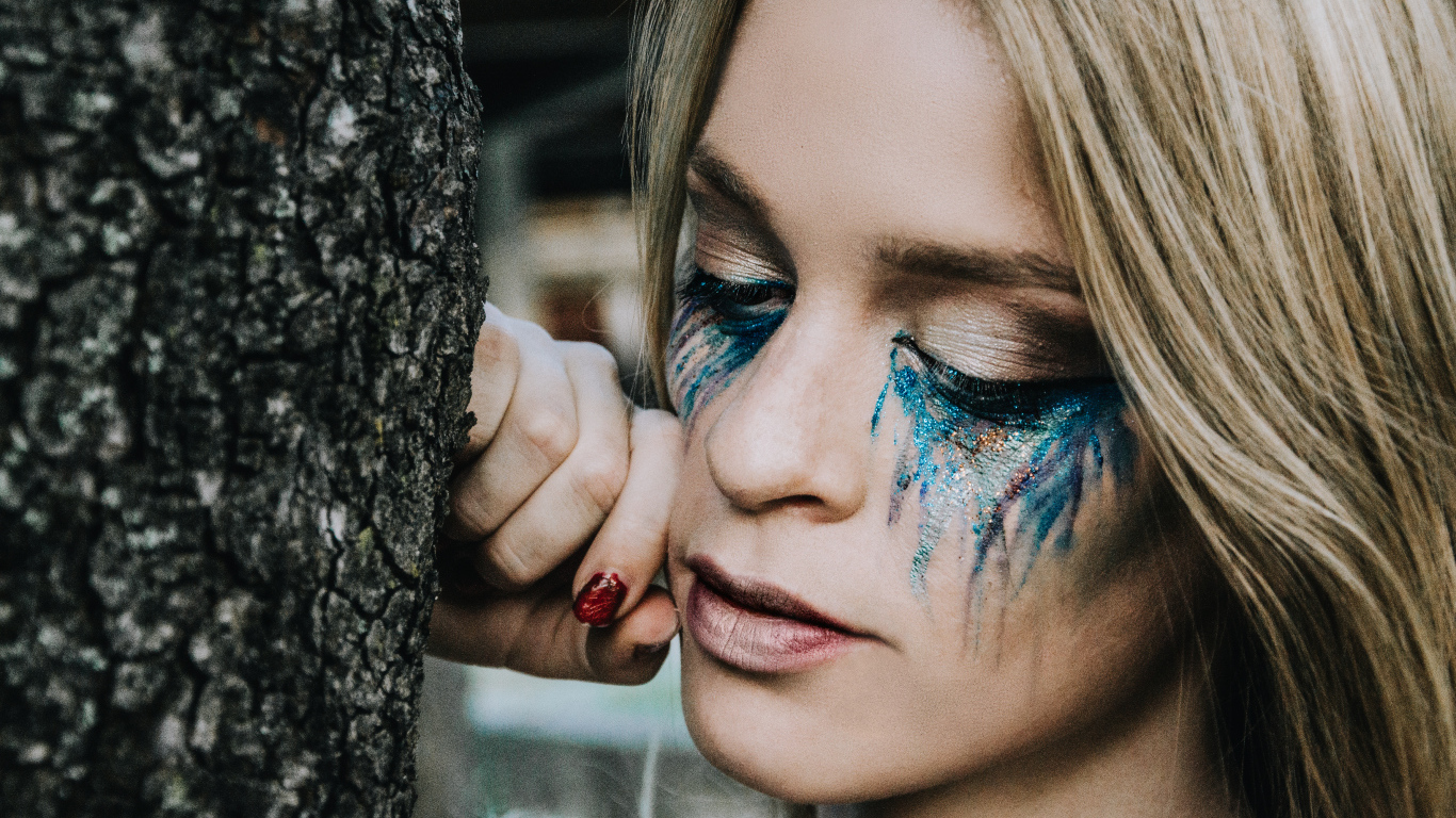 Заплаканная блондинка стоит у дерева