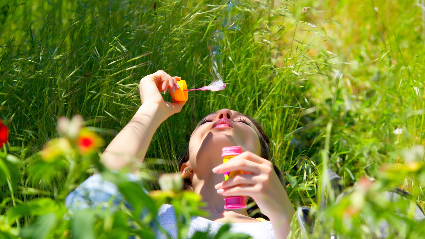 Молодая девушка лежит на зеленой траве с мыльными пузырями