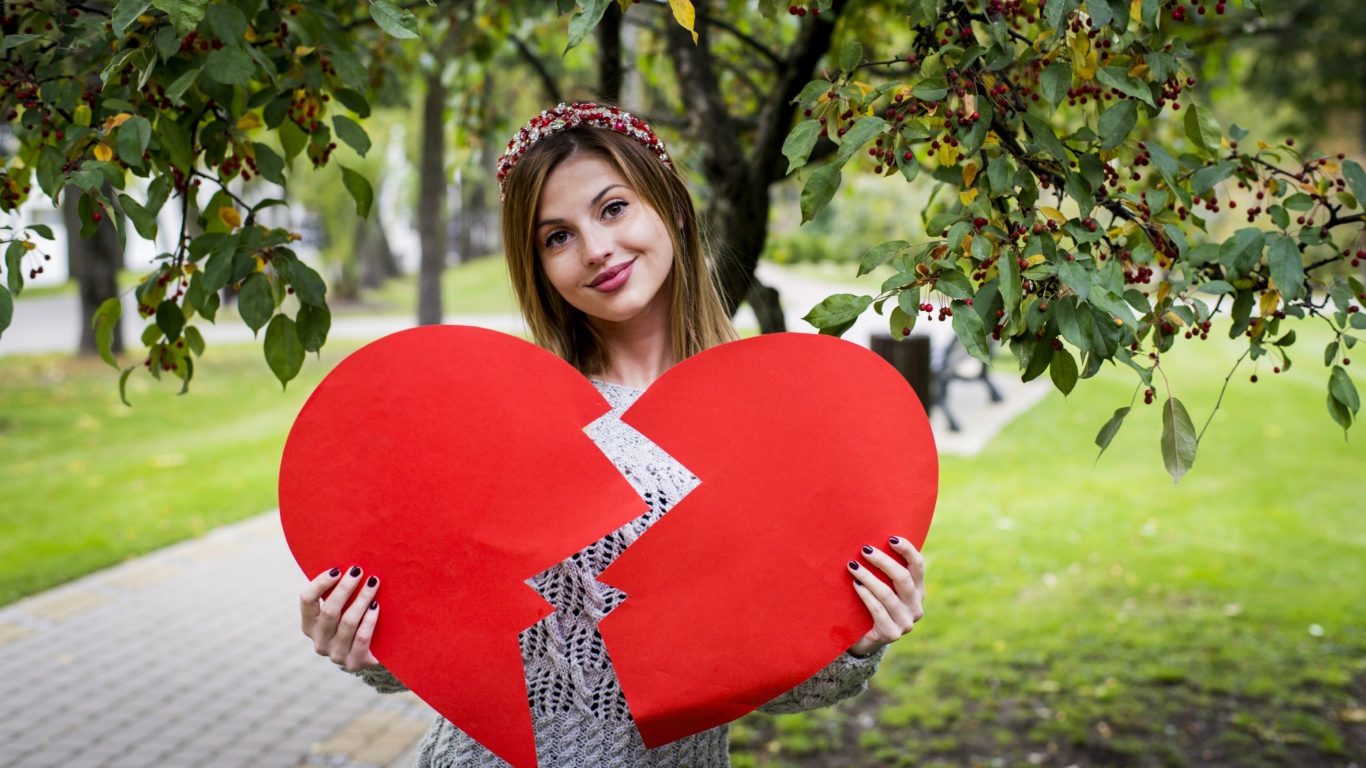 Молодая девушка с разбитым красным сердцем в руках