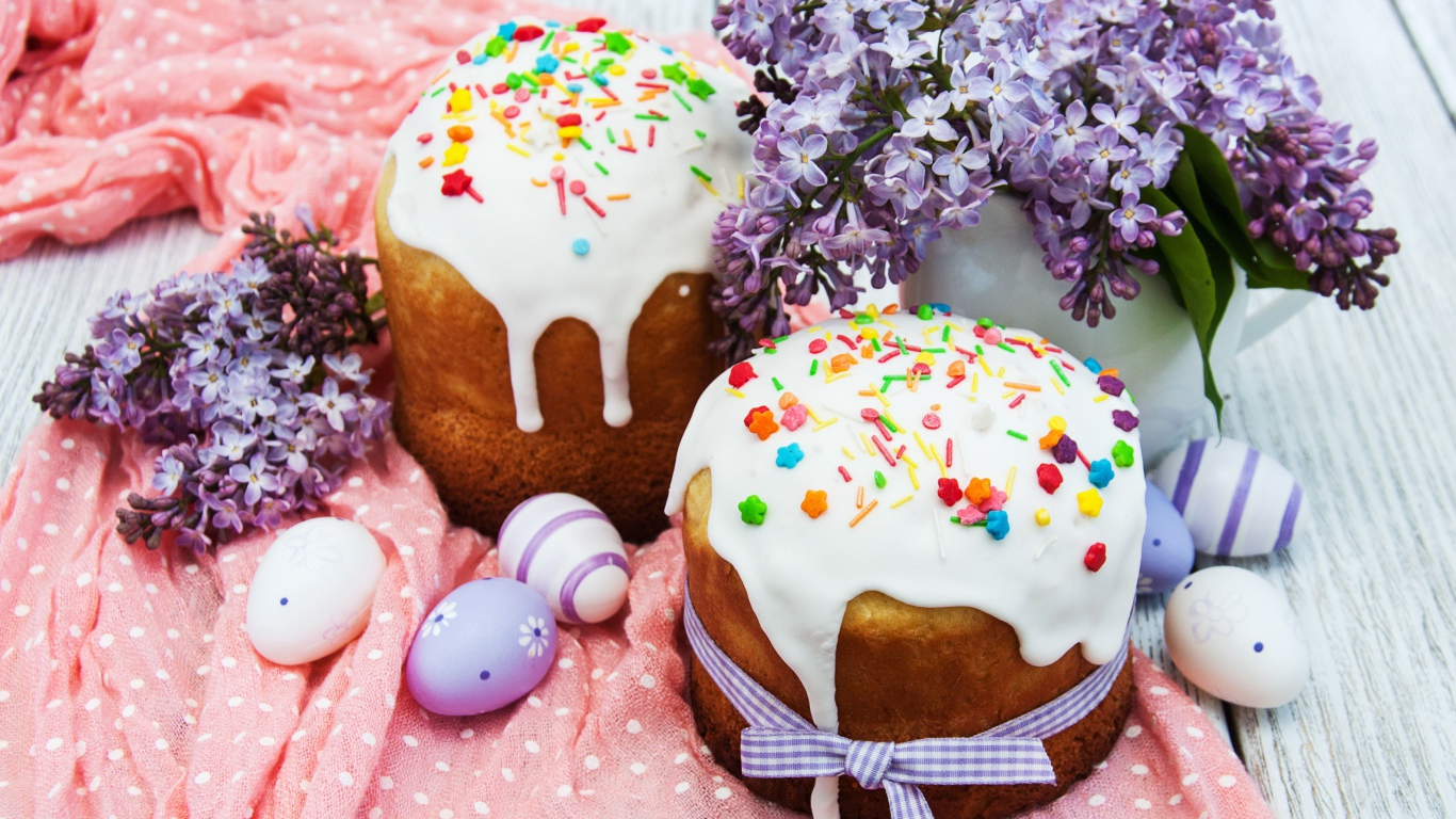 Пасхальные куличи с сахарной глазурью на столе с крашеными яйцами и букетом сирени на Пасху