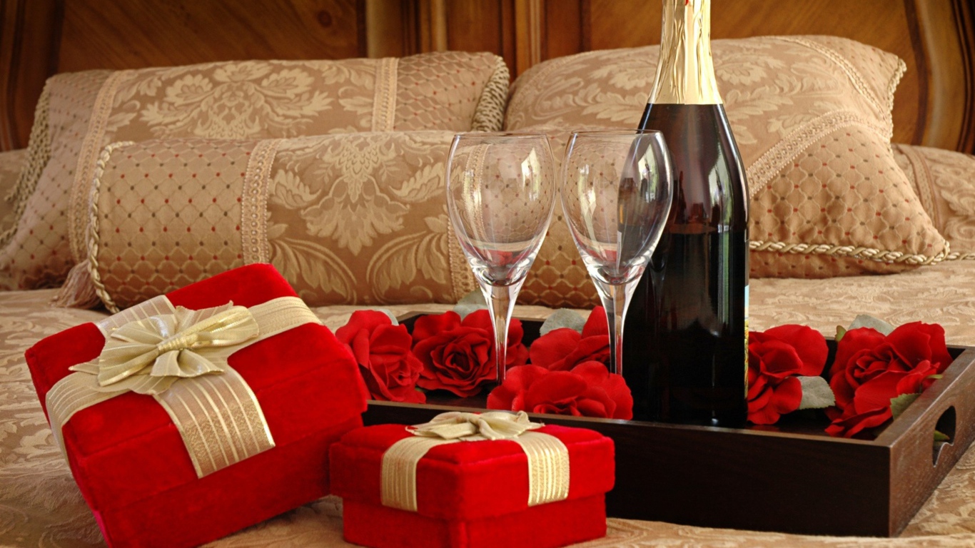 Бутылка вина, два бокала и подарки для романтического вечера на кровати 