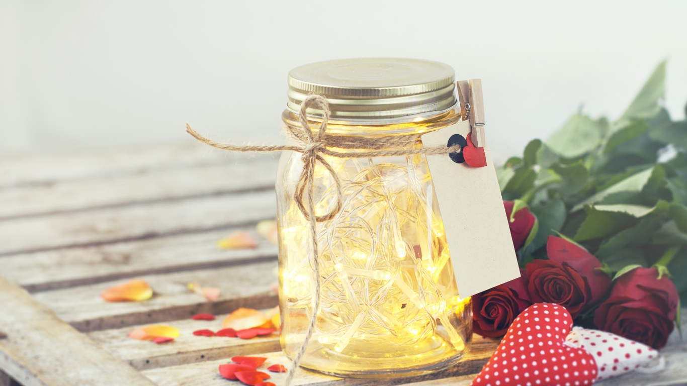 Стеклянная банка с гирляндой на столе с букетом роз и сердечками
