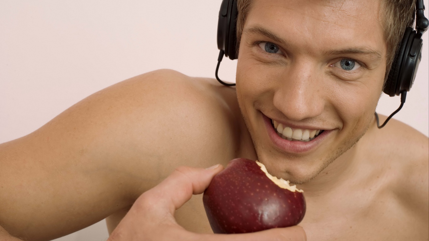 Красивый голубоглазый парень в наушниках с яблоком в руке