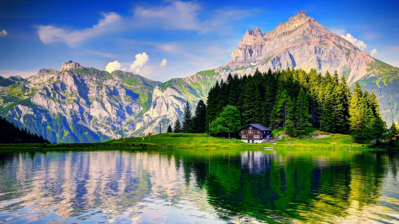 Forest and mountains are reflected in the lake under a beautiful blue sky with white clouds