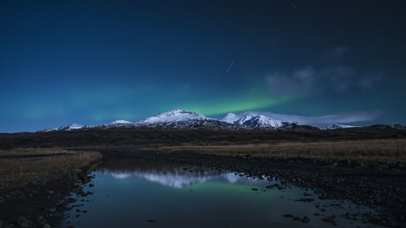 Горы и небо отражаются в луже на дороге ночью 
