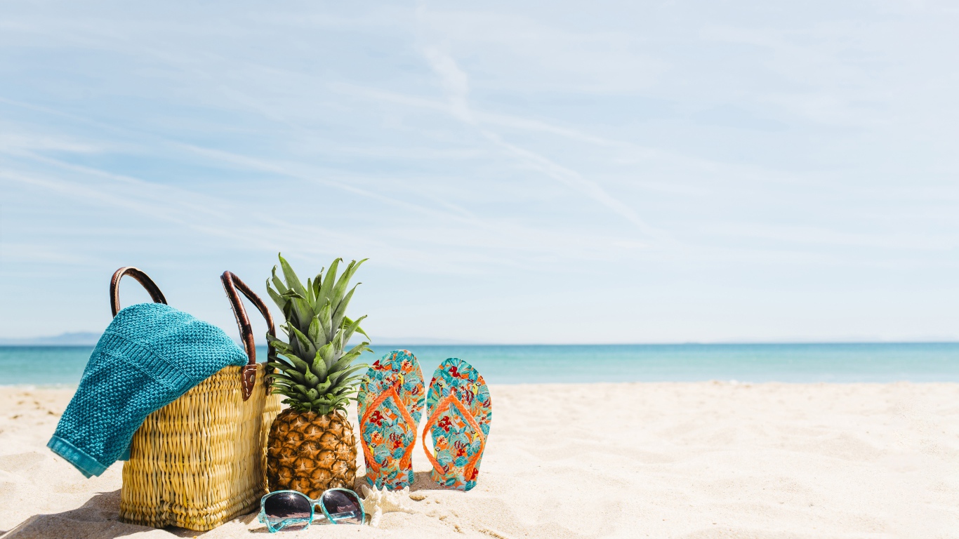 Сумка, ананас, шлепанцы и солнечные очки лежат на песке на пляже летом