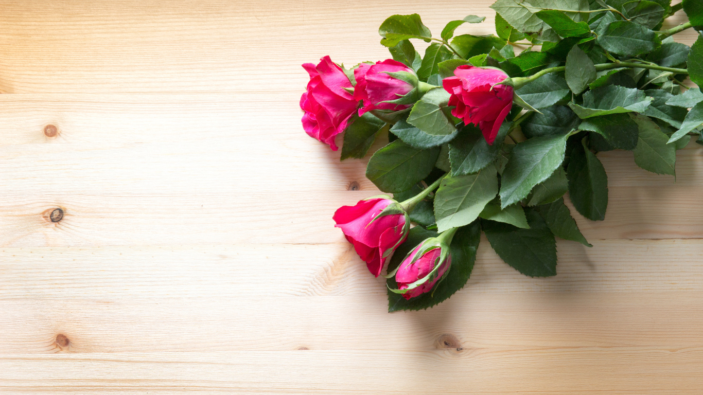Букет розовых роз с зелеными листьями на деревянной поверхности 