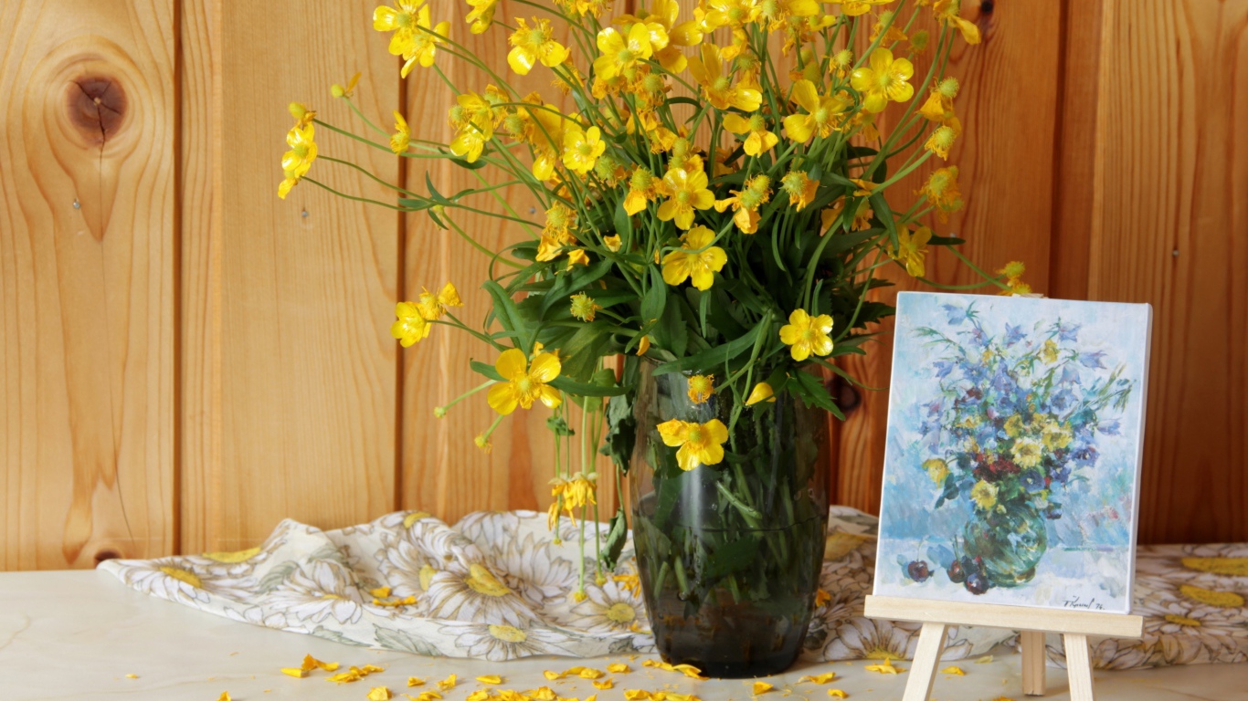 Букет желтых полевых лютиков в стеклянной вазе на столе с картиной