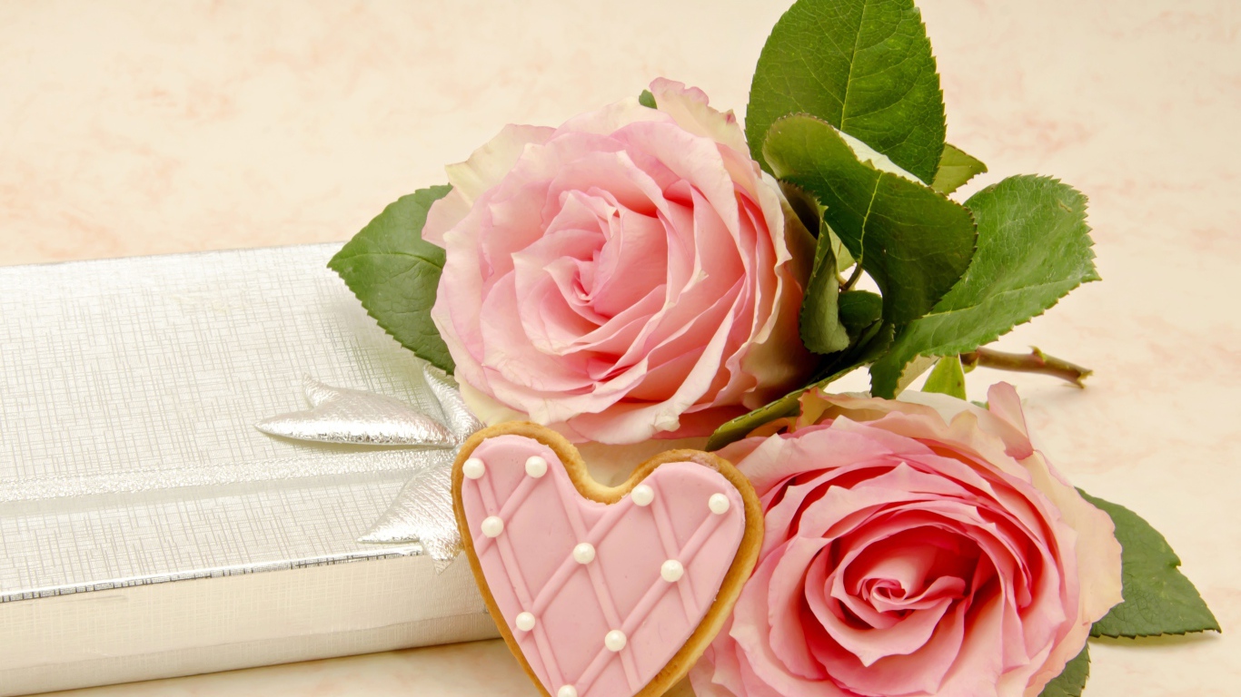 Две розовые розы с печеньем в виде сердца на розовом фоне