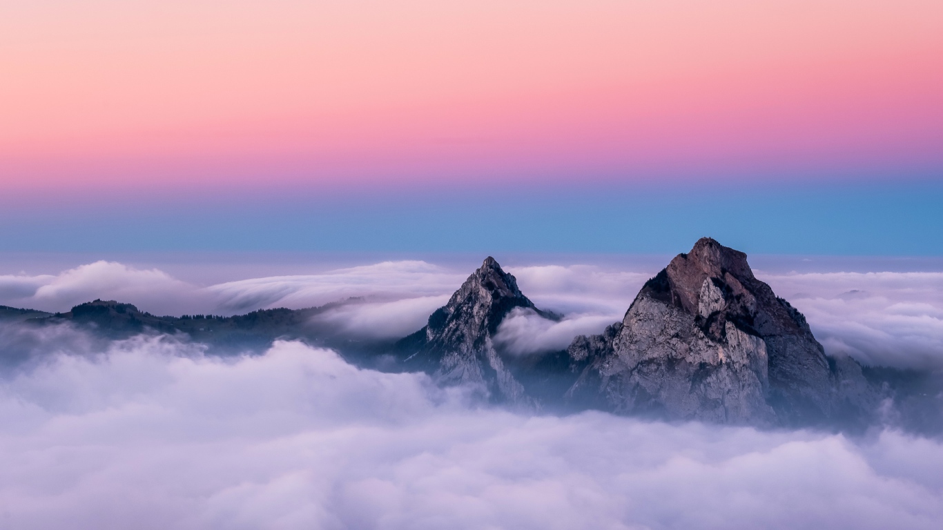 The tops of the mountains in white clouds under a beautiful pink sky