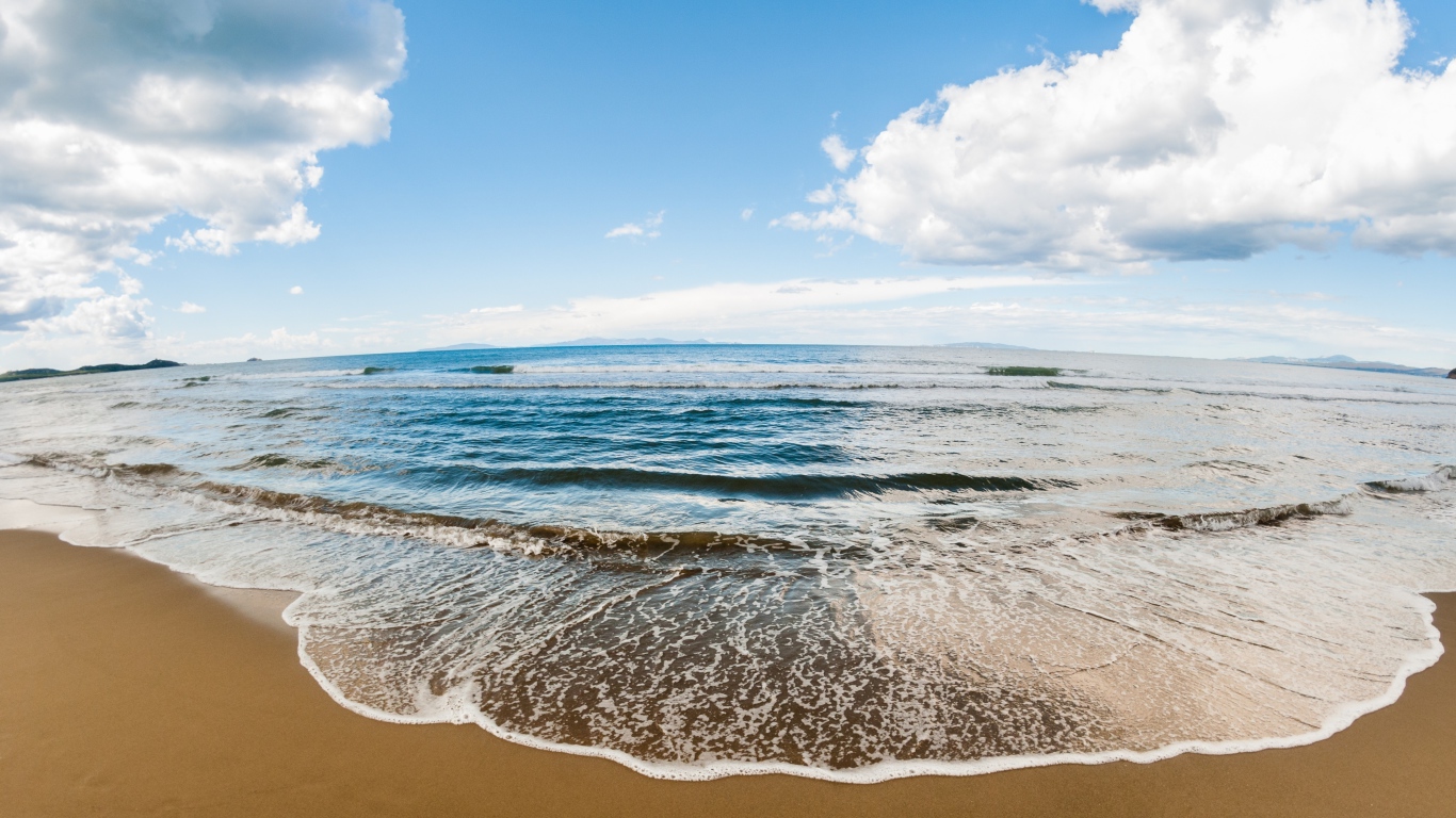 Морская волна на песке под красивым небом с белыми облаками