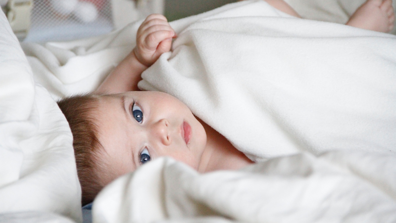 Маленький голубоглазый мальчик под белым покрывалом