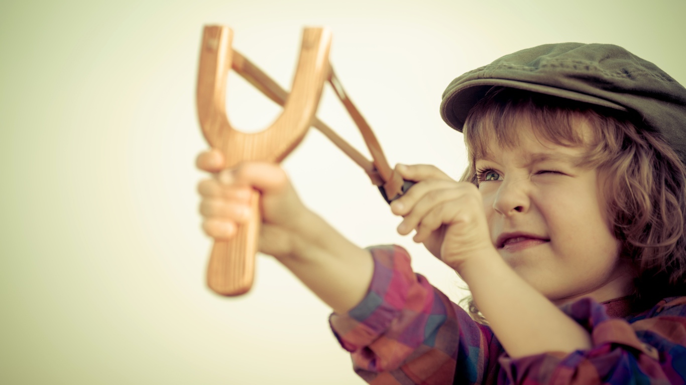 Маленький мальчик в кепке целится с рогатки