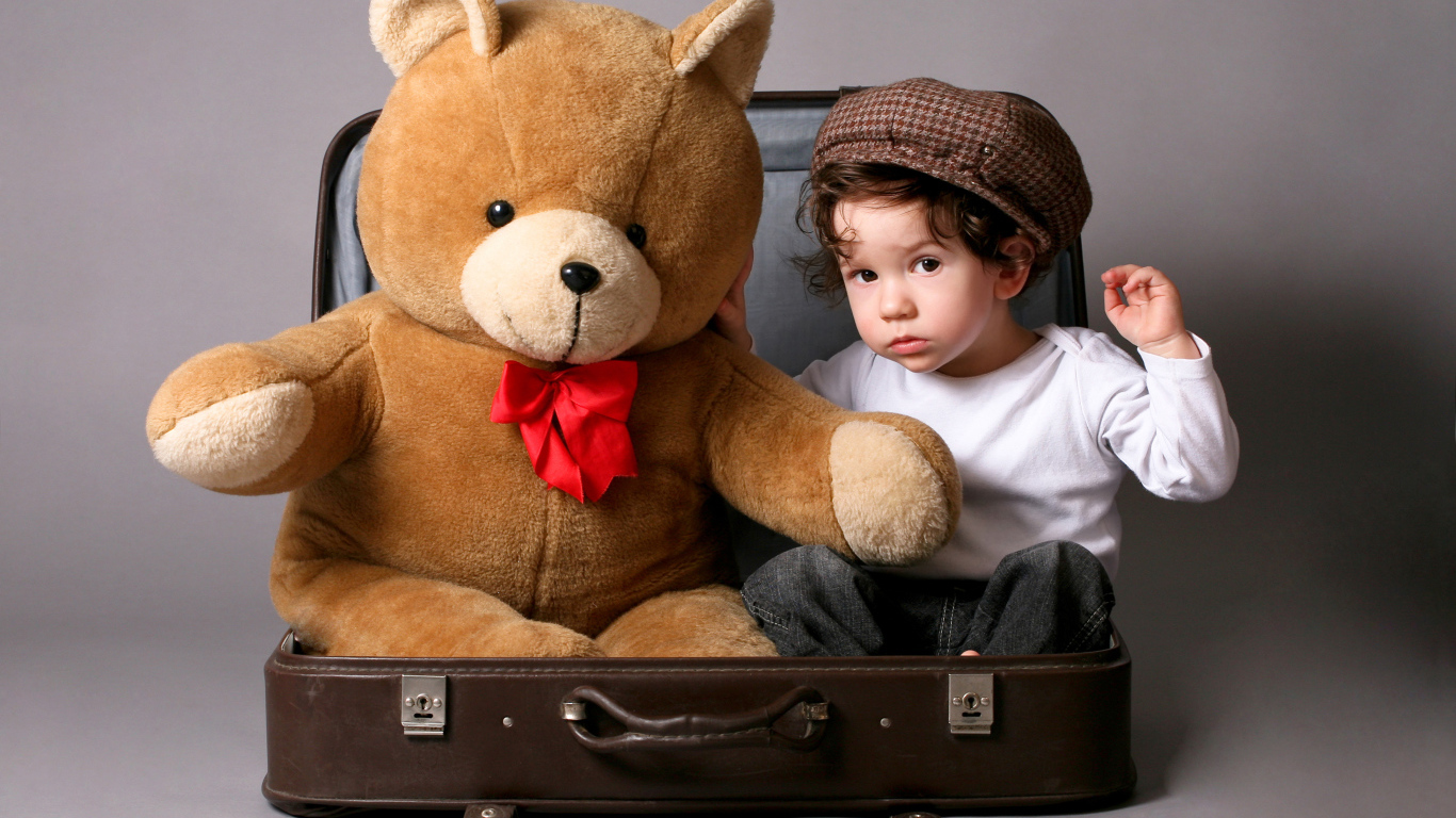 Маленький мальчик сидит в чемодане с плюшевым мишкой 