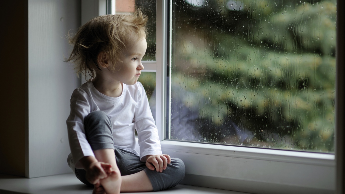 Маленькая девочка сидит на подоконнике у окна