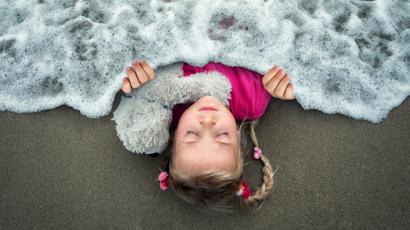 Маленькая девочка спит на песке под одеялом из морской пены