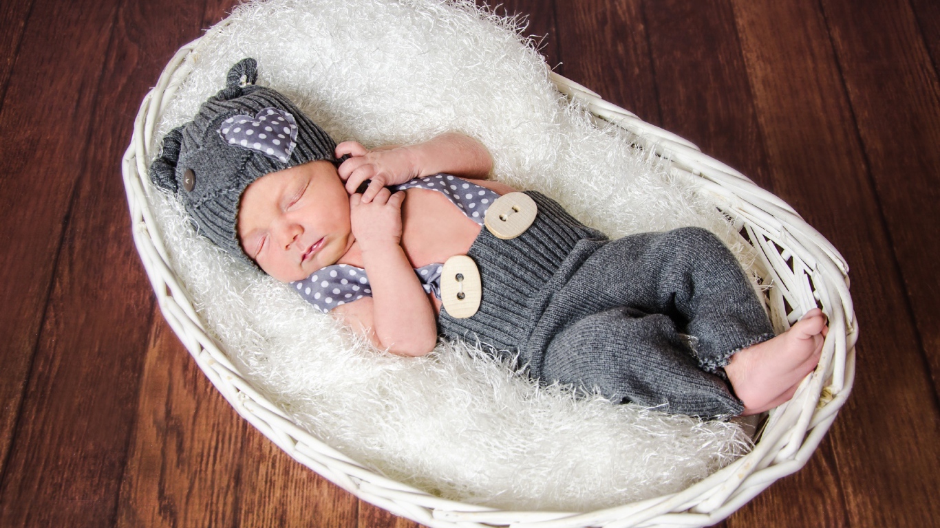 Спящий младенец в сером костюме в белой корзине