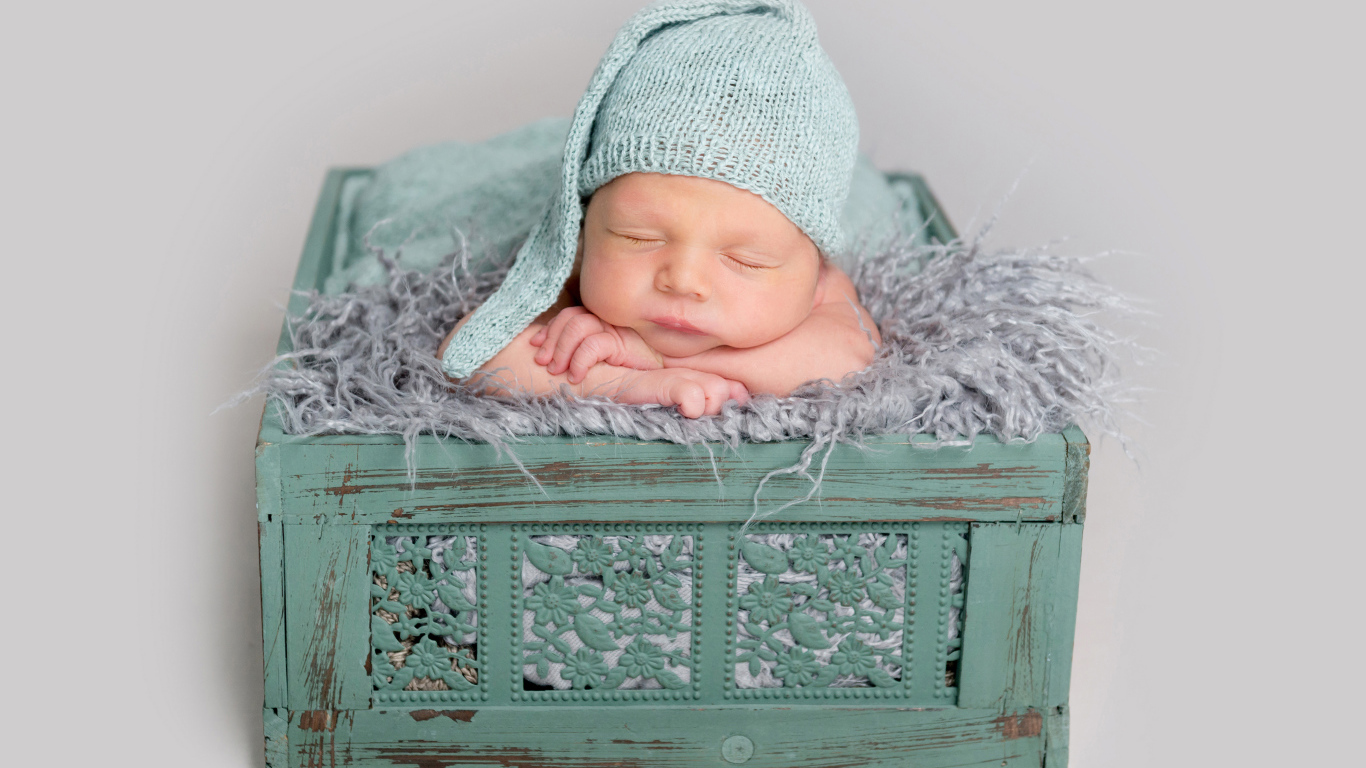 Спящий ребенок в зеленом ящике на сером фоне