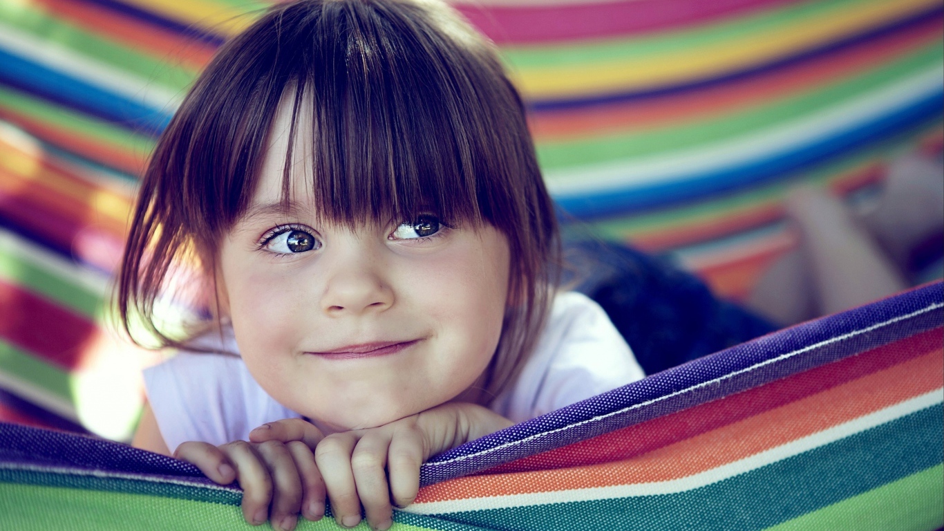 Маленькая кареглазая девочка лежит в гамаке