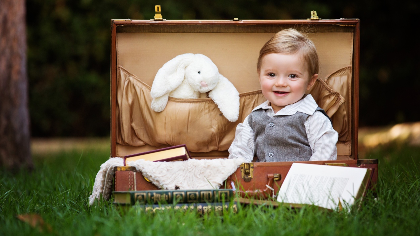 Улыбающийся мальчик сидит в чемодане с книгами