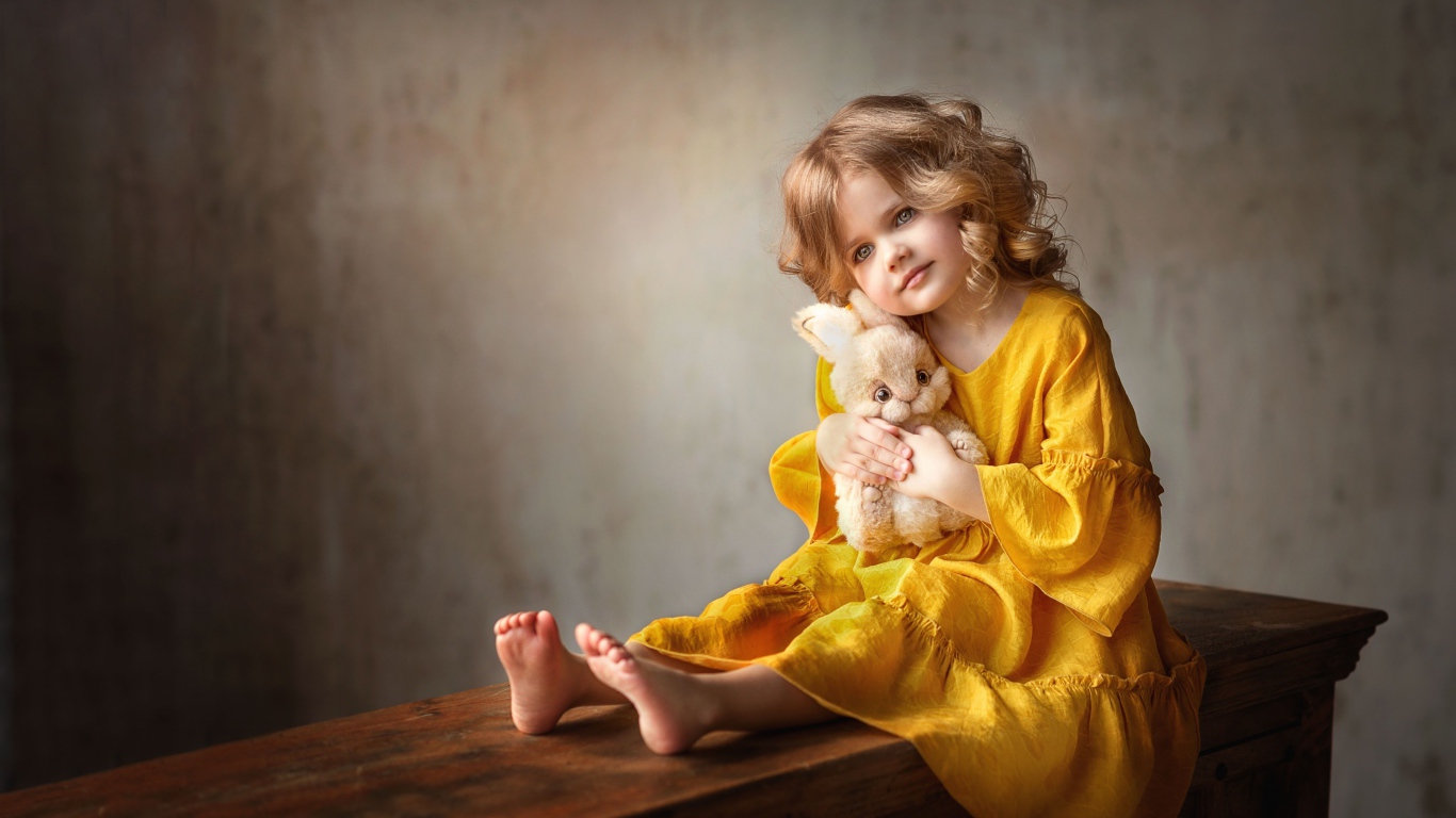 Красивая маленькая девочка в желтом платье с игрушкой