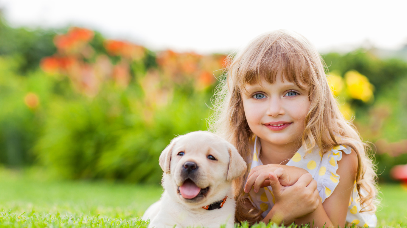 Милая маленькая девочка с щенком золотистого ретривера лежит на зеленой траве